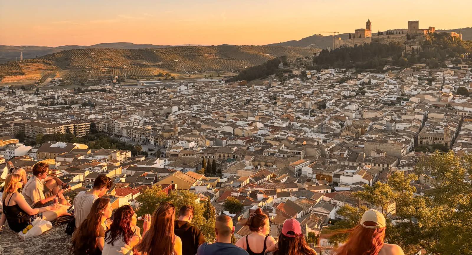 Grupo de jóvenes sentados en un mirador viendo el atardecer sobre una ciudad española
